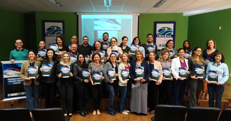 Grupo de pessoas no palco com a publicação do Programa Estadual de Educação ambiental nas mãos.