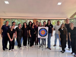 Foto mostra a equipe do CRAS/Imasul reunida durante a XVI Semana Científica de Medicina Veterinária. O grupo, formado por homens e mulheres, posa em um espaço interno ao lado de um alvo de arco e flecha, sorrindo para a câmera. A maioria veste uniforme escuro, em clima de integração e atividade científica.